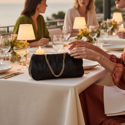 Woman sitting at a dinner table with a black handbag, engaged in conversation with others.