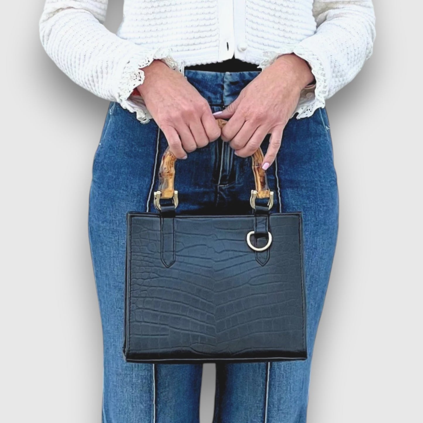 Shop Sarah Stewart Clara mini handbag in black goat skin with bamboo handles and gold hardware held by a woman.