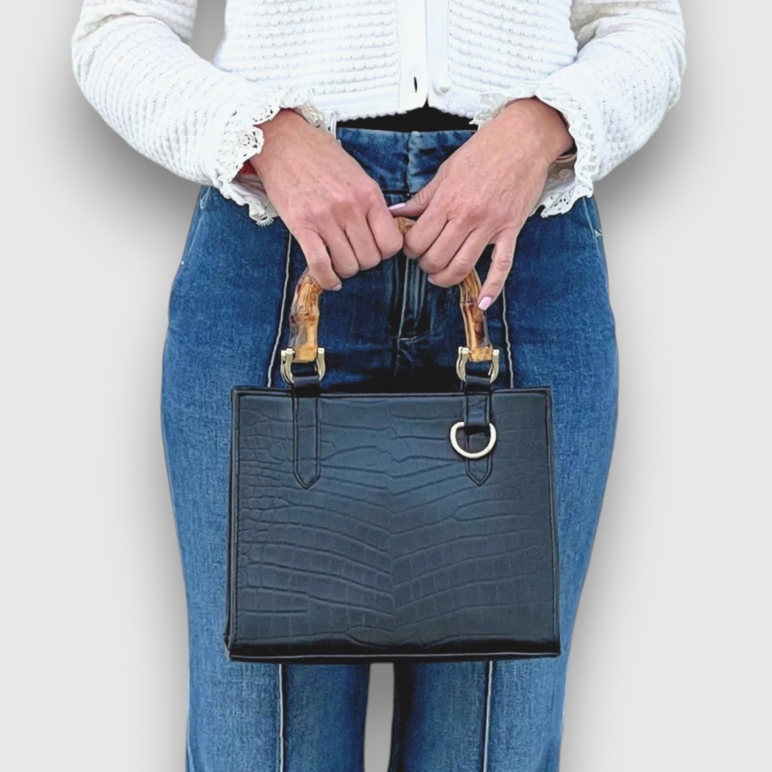 Shop Sarah Stewart Clara mini handbag in black goat skin with bamboo handles and gold hardware held by a woman.
