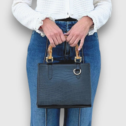 Shop Sarah Stewart Clara mini handbag in black goat skin with bamboo handles and gold hardware held by a woman.
