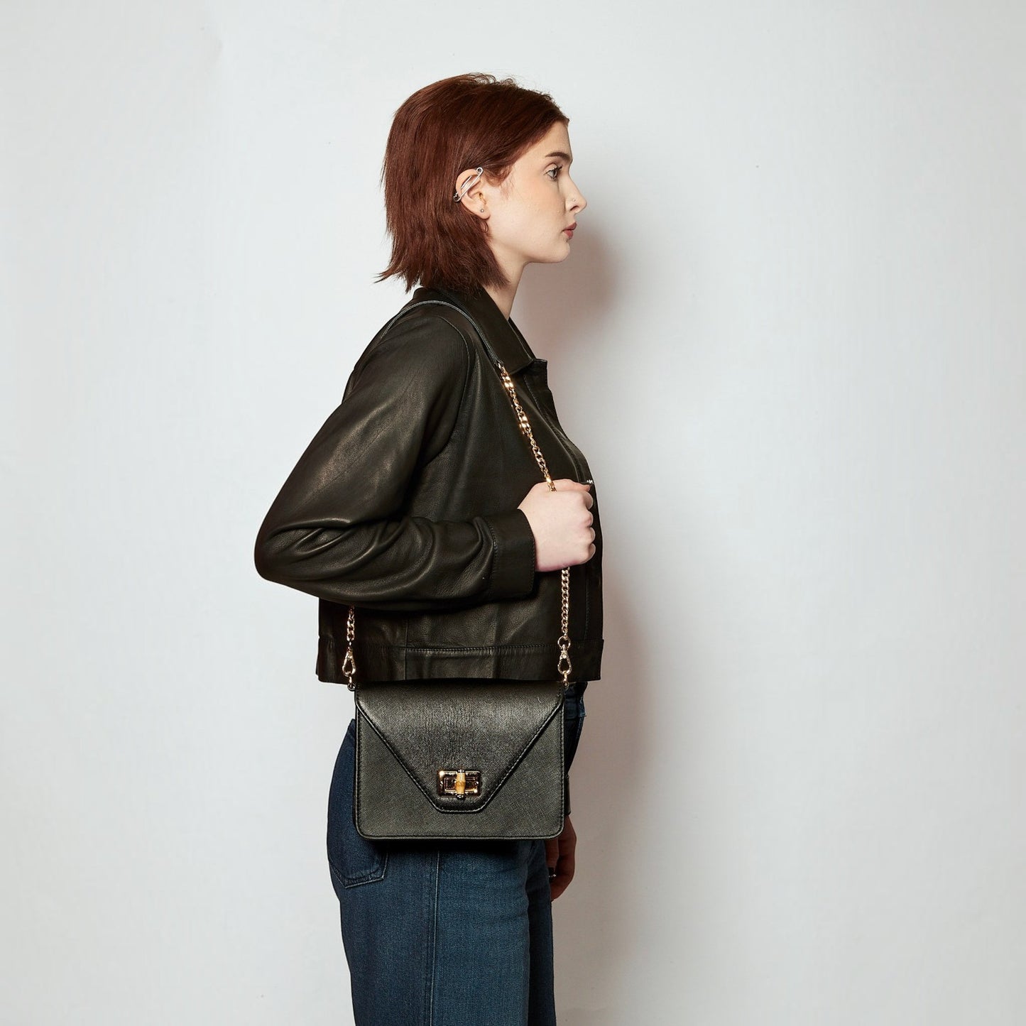 Model wearing a Shop Sarah Stewart black saffiano leather shoulder bag with a bamboo closure and gold chain strap.