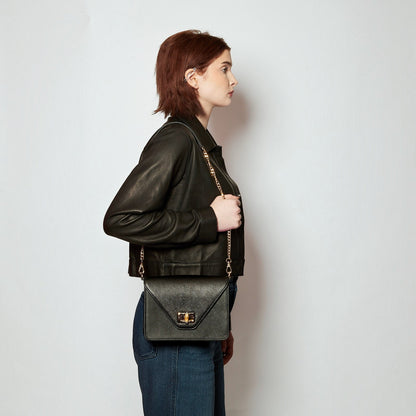 Model wearing a Shop Sarah Stewart black saffiano leather shoulder bag with a bamboo closure and gold chain strap.