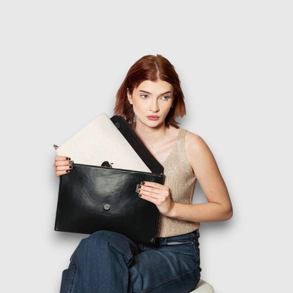 Shop Sarah Stewart black vegan leather Lisa laptop clutch with gold chain strap held by a woman in a gold top
