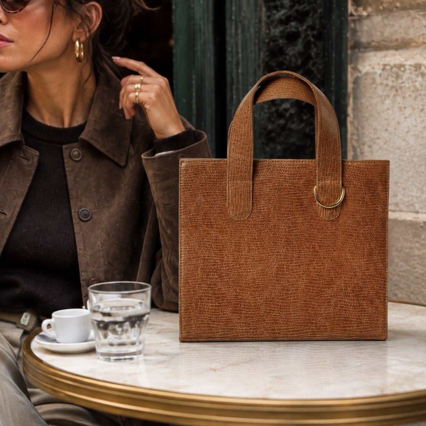 Shop Sarah Stewart Claire Maxi structured brown embossed goatskin leather handbag on a cafe table