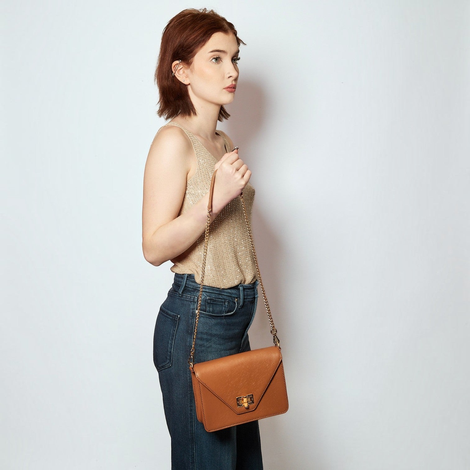 Shop Sarah Stewart The Stacey Stefano brown leather crossbody bag with chain strap worn by a woman in a gold top