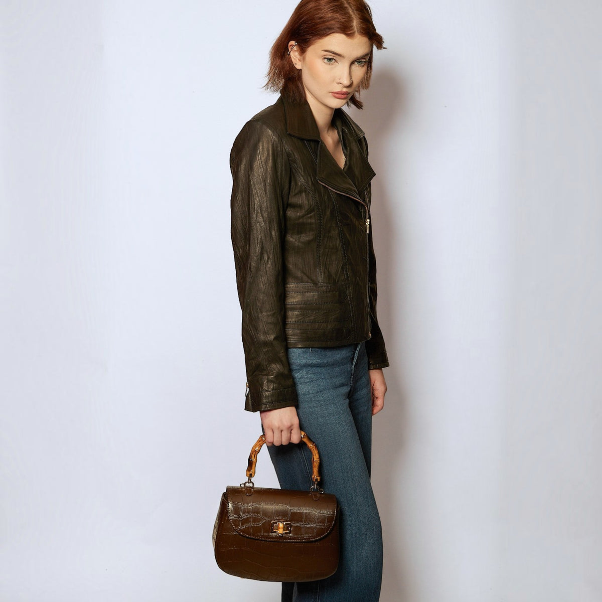 Model holding a Shop Sarah Stewart brown embossed goat skin suede handbag with a bamboo handle and gold closure.