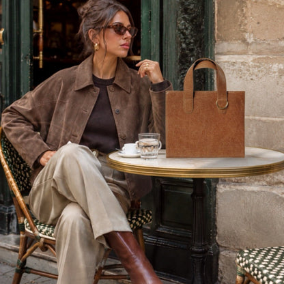 Shop Sarah Stewart Claire Maxi brown embossed goatskin leather tote bag with gold hardware on a cafe table