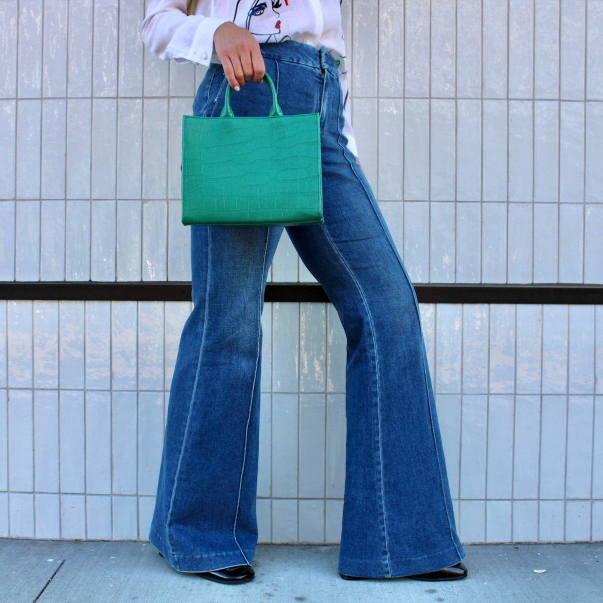 Shop Sarah Stewart Adelaide handbag in green embossed goat skin leather held by a model in flared blue jeans
