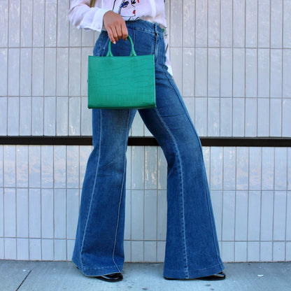Shop Sarah Stewart Adelaide handbag in green embossed goat skin leather held by a model in flared blue jeans