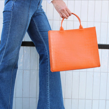 Shop Sarah Stewart Adele handbag in bright orange embossed croc lambskin leather held by a person in blue jeans.