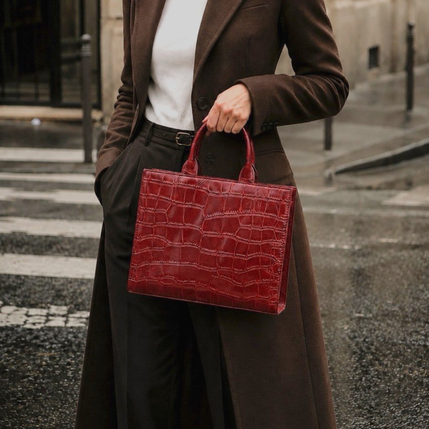 Shop Sarah Stewart Adele handbag in deep red embossed croc leather held by a woman in a brown coat on a city street.