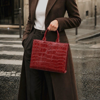 Shop Sarah Stewart Adele handbag in deep red embossed croc leather held by a woman in a brown coat on a city street.
