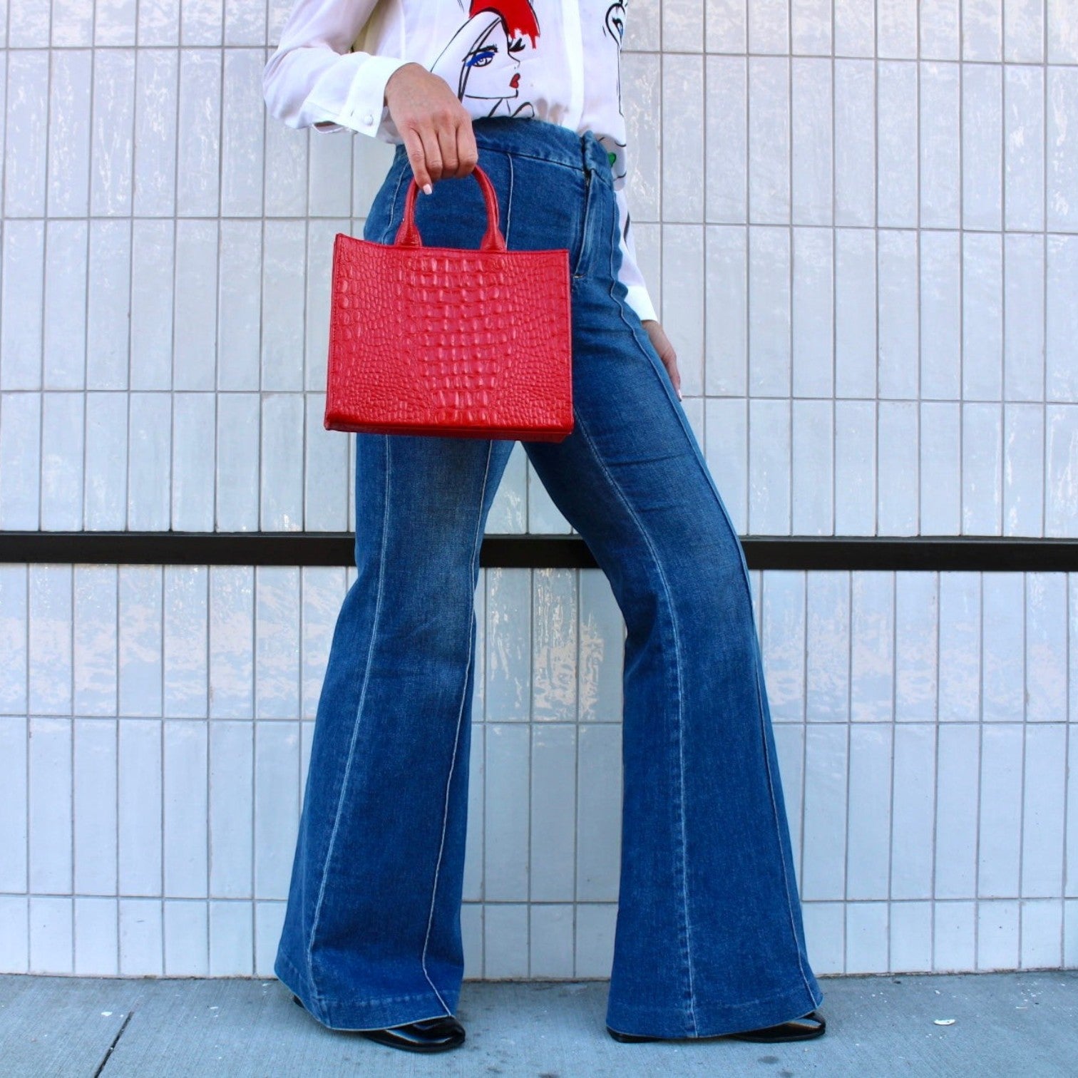 Shop Sarah Stewart red embossed crocodile leather Adelaide handbag held by a woman in flared jeans and white shirt