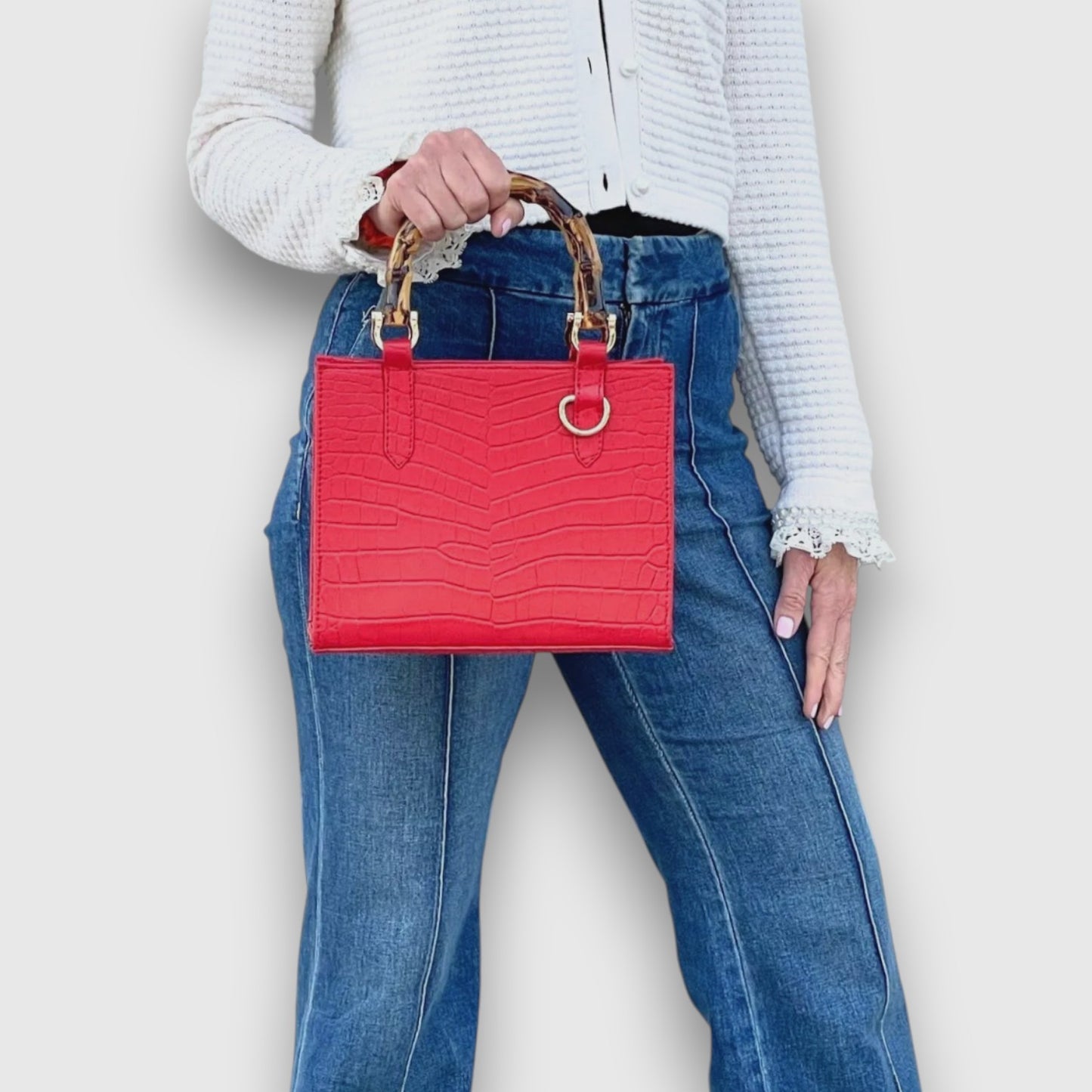 Shop Sarah Stewart red goat skin mini handbag with bamboo handles and gold hardware held by a woman in jeans