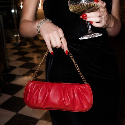 Shop Sarah Stewart Amina red pleated lambskin leather clutch bag with gold chain strap held by a woman in a black dress