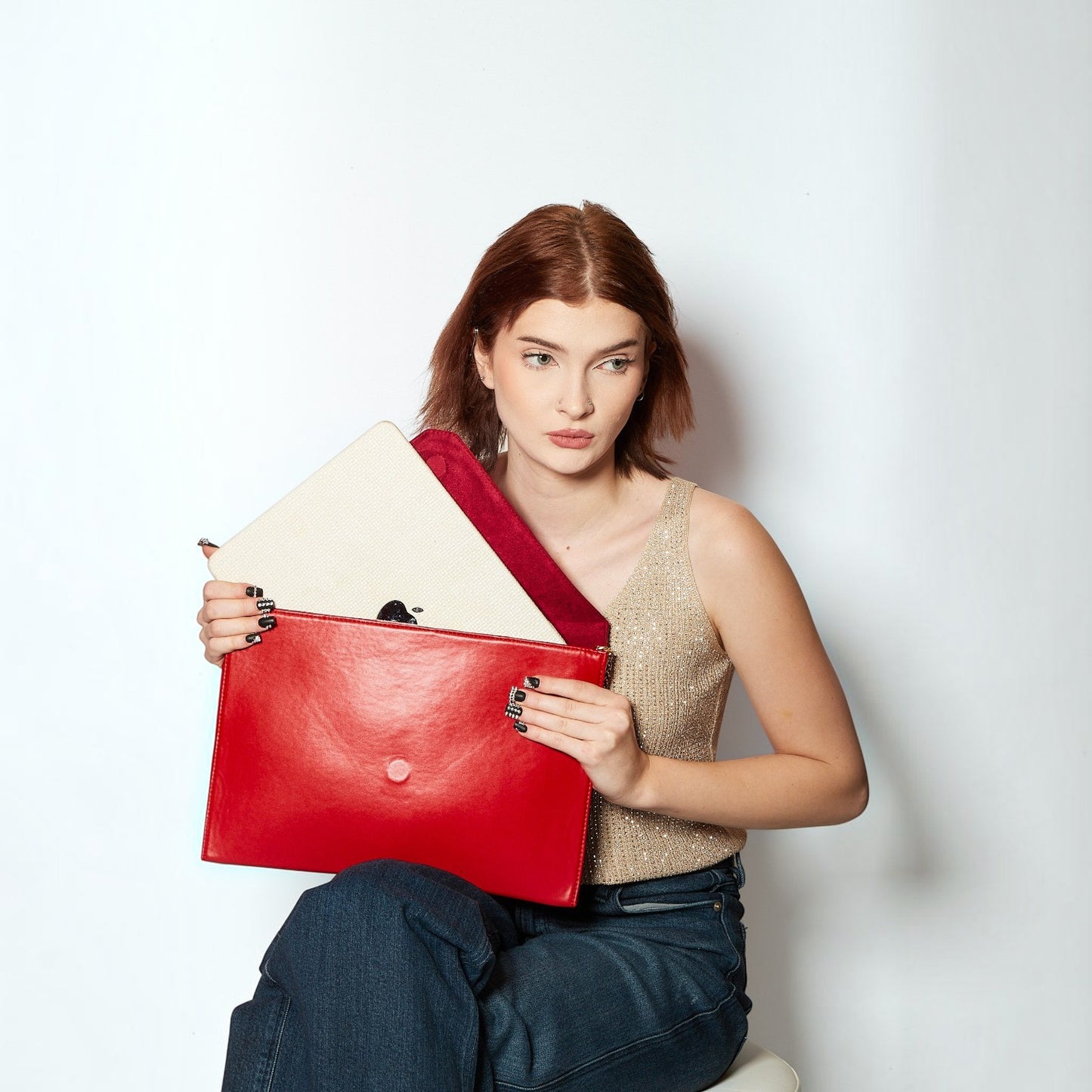 Shop Sarah Stewart Lisa laptop clutch in red vegan leather with a beige interior, held by a woman in a gold top.
