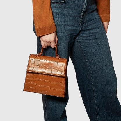 Shop Sarah Stewart The Robin handbag in brown crocodile-embossed goat skin leather with gold hardware held by hand