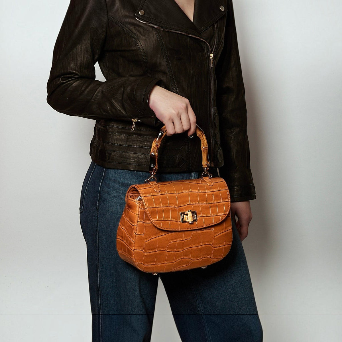 Shop Sarah Stewart The Chloe tan embossed goat skin suede handbag with bamboo handle and gold closure held by a model