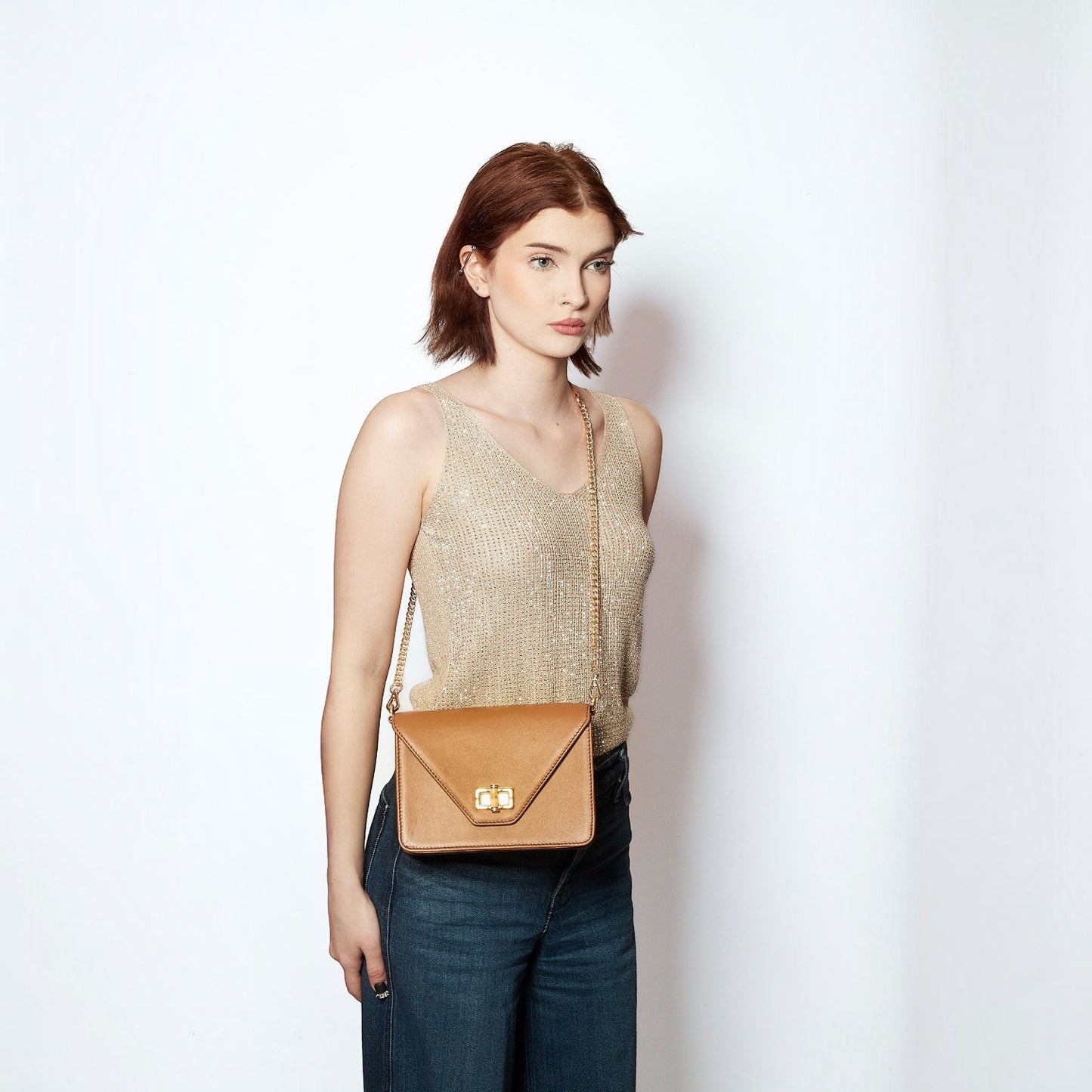 Model wearing a Shop Sarah Stewart Stacey Stefano tan leather crossbody bag with a gold chain and bamboo closure
