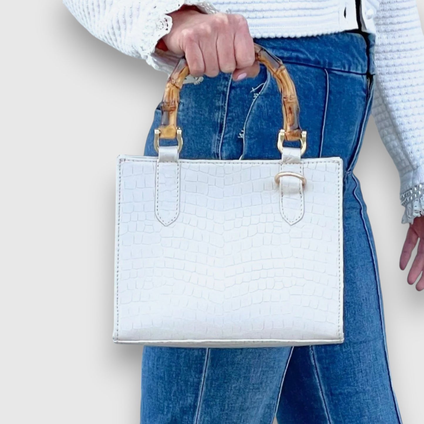 Shop Sarah Stewart white goat skin Clara mini handbag with bamboo handles and gold hardware held by a woman